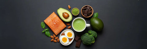 Matcha tea with keto-friendly foods like avocado, eggs, salmon, nuts, and greens on a dark background