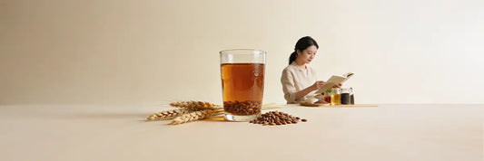 A cup of mugicha barley tea beside scattered roasted barley grains, with a gluten-free awareness ribbon