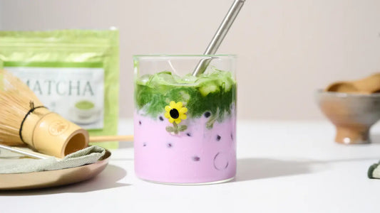 ube matcha latte with two-layered of matcha tea and purple ube  in a glass with a straw on a textured surface.