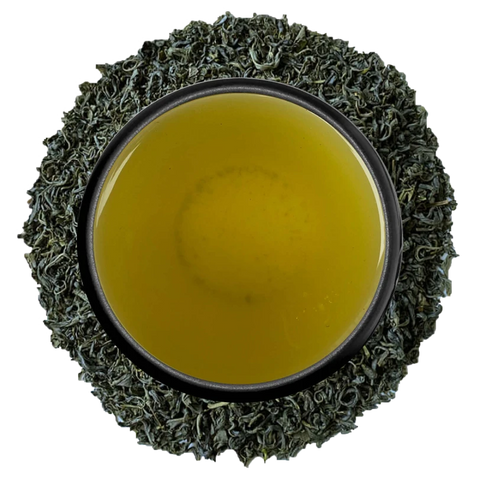A cup of clear yellow kamairicha seen from above, ringed by curled pan-fired leaves on a white background
