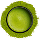 A bowl of whisked bright green matcha seen from above, ringed by matcha powder on a white background